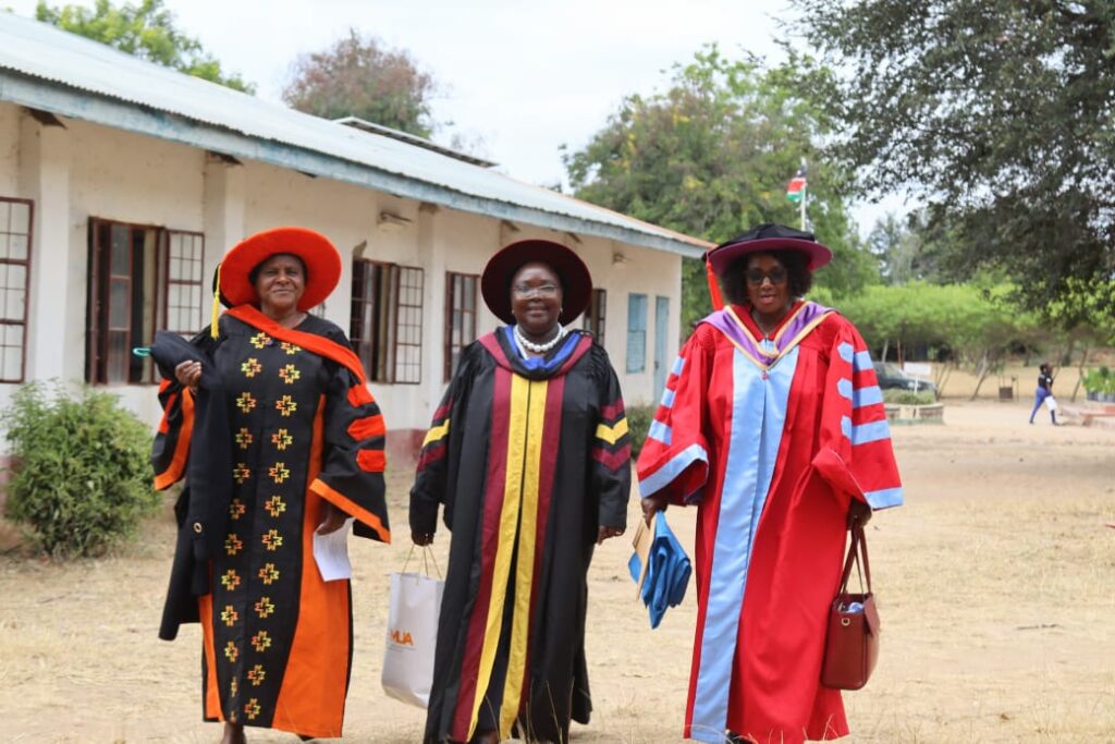 Three female members of the Kitui Dons Association walking in their vibrant and colorful academic gowns and hats during the event.