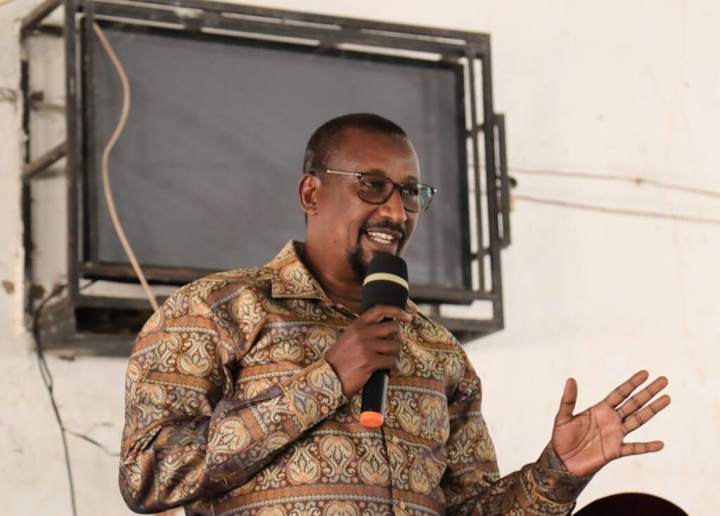Dr. Mohamed Abdinoor Dahir delivering an engaging speech into a microphone during the Kitui East Sub-County academic clinic at St. Mary Mutito Girls.